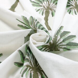 Peut inclure: Tissu blanc avec un imprim&eacute; de palmier vert et marron. Le tissu est pli&eacute; et tordu, montrant le motif.