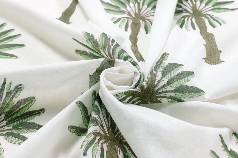Peut inclure: Tissu blanc avec un imprim&eacute; de palmier vert et marron. Le tissu est pli&eacute; et tordu, montrant le motif.