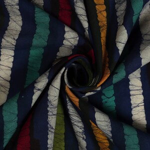 May include: A close-up of a blue fabric with colorful stripes. The fabric has a batik pattern with white lines and a textured look. The fabric is folded and twisted, showing the different colors and patterns.