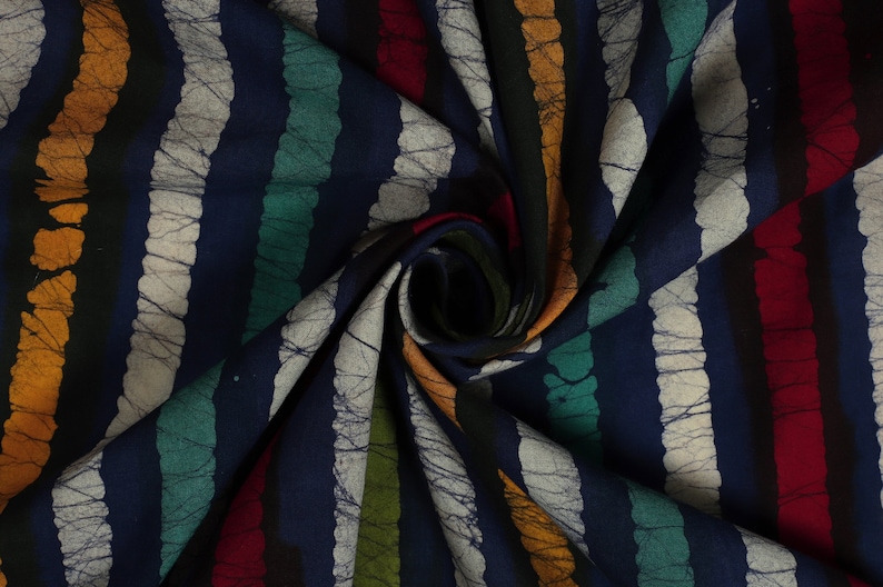 May include: A close-up of a blue fabric with colorful stripes. The fabric has a batik pattern with white lines and a textured look. The fabric is folded and twisted, showing the different colors and patterns.