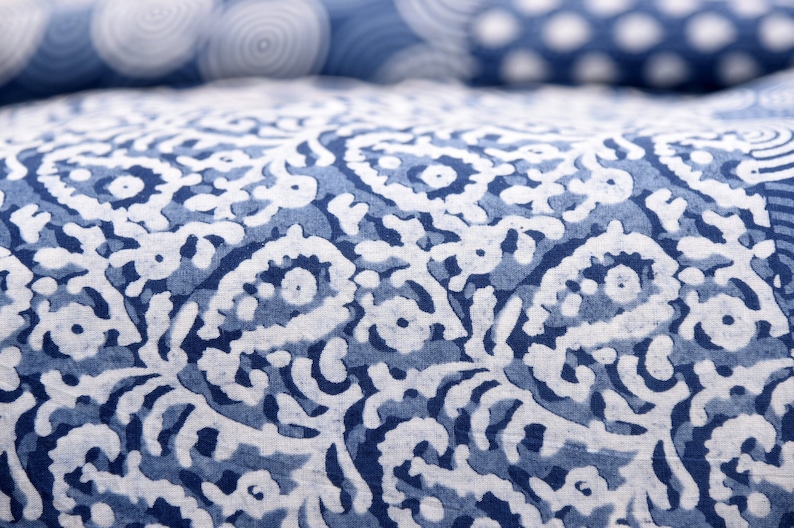 Op de afbeelding: Close-up van een blauwe en witte stof met een herhalend patroon van gestileerde bloemen. De stof voelt zacht en textuurrijk aan.