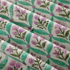 May include: A close-up of a white fabric with a repeating pattern of pink flowers and green leaves. The fabric has a subtle sheen and a soft texture.