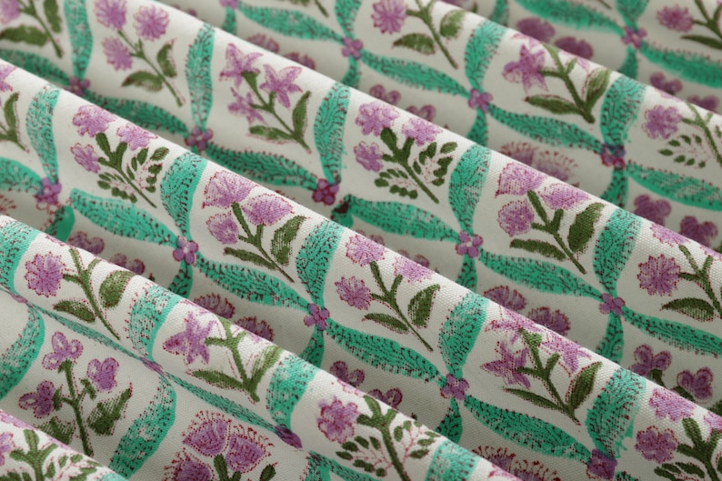 May include: A close-up of a white fabric with a repeating pattern of pink flowers and green leaves. The fabric has a subtle sheen and a soft texture.