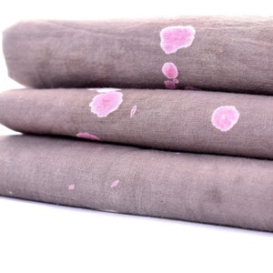 May include: A stack of three gray fabric napkins with pink splotches. The napkins are folded and stacked on top of each other.