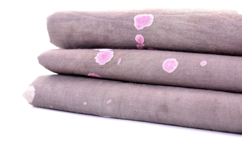 May include: A stack of three gray fabric napkins with pink splotches. The napkins are folded and stacked on top of each other.