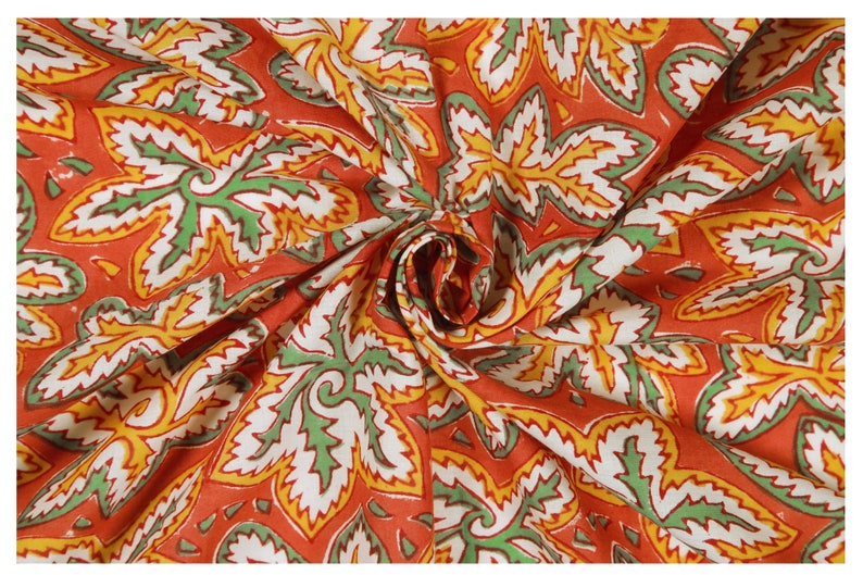 Pode incluir: Tecido vermelho com um padr&atilde;o floral branco, verde e amarelo. O tecido est&aacute; dobrado e tem uma superf&iacute;cie texturizada.