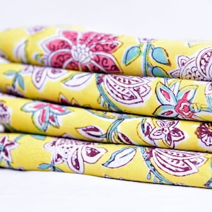 May include: A stack of four yellow fabric napkins with a floral print in shades of pink, purple, and blue.