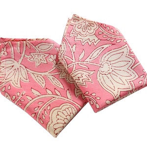Op de afbeelding: Twee roze stoffen servetten met een wit bloemenpatroon. De servetten zijn dubbelgevouwen en liggen op een witte achtergrond.