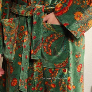May include: A green velvet robe with a floral print in shades of orange, red, and yellow. The robe has a self-tie belt and two pockets.