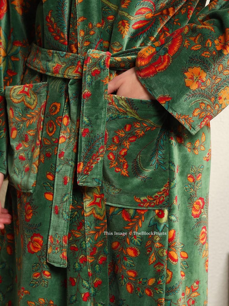 May include: A green velvet robe with a floral print in shades of orange, red, and yellow. The robe has a self-tie belt and two pockets.