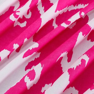 Op de afbeelding: Roze en witte stof met een herhalend abstract patroon. De stof is gevouwen en heeft een zachte, vloeiende textuur.
