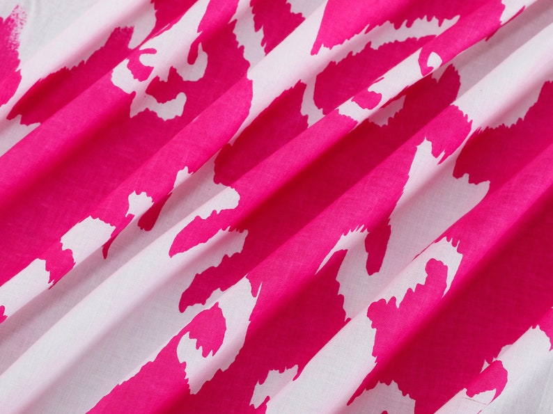 Op de afbeelding: Roze en witte stof met een herhalend abstract patroon. De stof is gevouwen en heeft een zachte, vloeiende textuur.