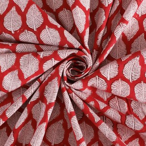 May include: Red fabric with a white leaf pattern. The fabric is folded and twisted, showing the pattern.
