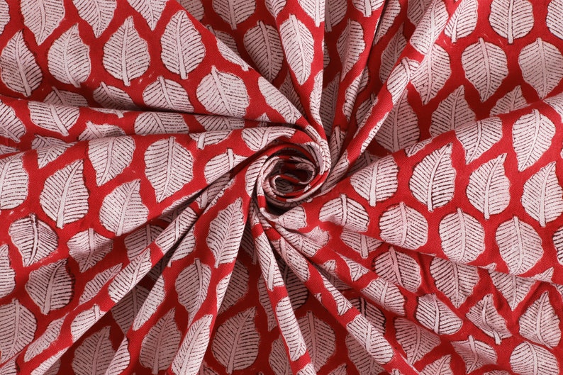May include: Red fabric with a white leaf pattern. The fabric is folded and twisted, showing the pattern.