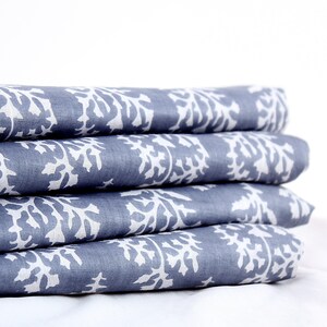 May include: A stack of four folded blue fabric pieces with a white floral pattern. The fabric is a solid blue color with a repeating white design. The fabric is folded neatly, with the edges aligned.