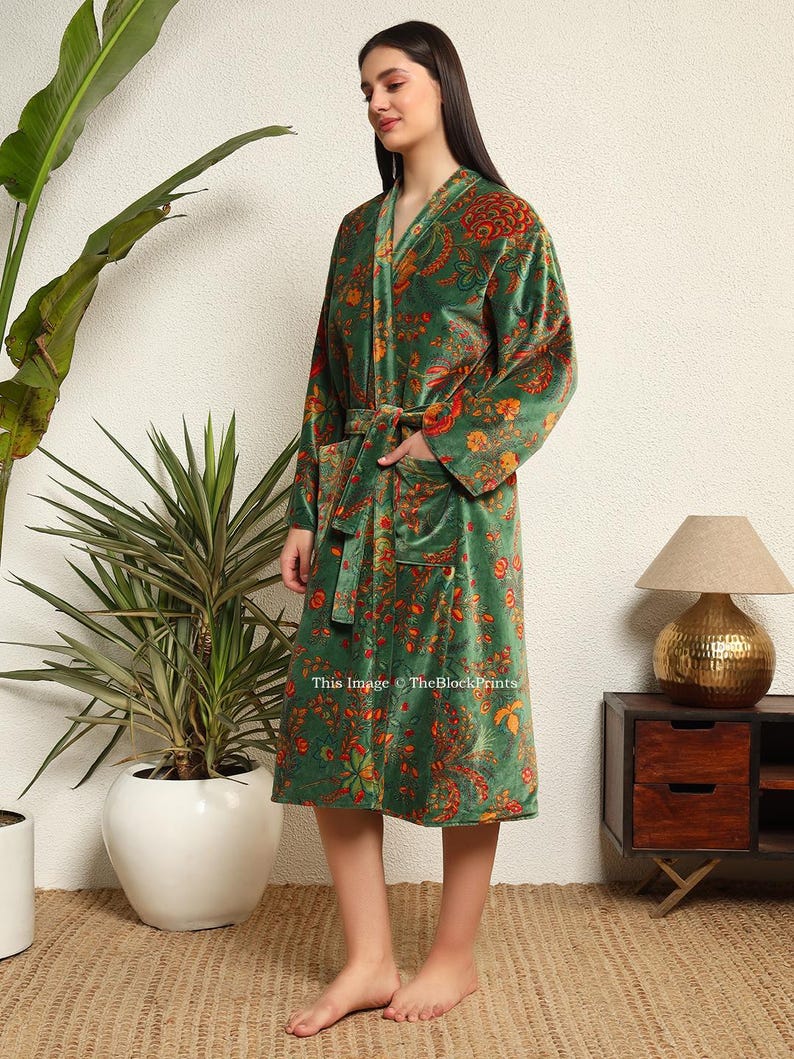 May include: A green velvet robe with a floral print and a self-tie belt. The robe has a long sleeve and a shawl collar.