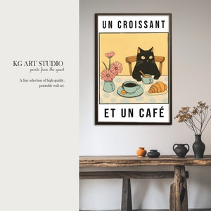 以下が含まれることがあります： 黒い猫が、コーヒーカップ、クロワッサン、ピンクの花束のあるテーブルに座っています。画像には「UN CROISSANT ET UN CAFÉ」というテキストが印刷されています。