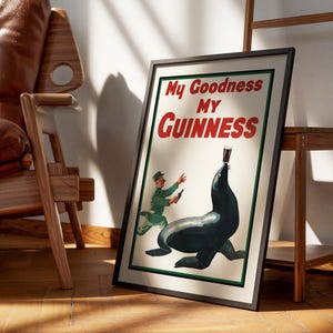 May include: Framed vintage Guinness advertisement featuring a seal balancing a pint of stout. The poster has the text "My Goodness My Guinness" in red and white. A man in a green uniform is running towards the seal.