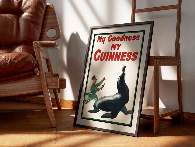 May include: Framed vintage Guinness advertisement featuring a seal balancing a pint of stout. The poster has the text "My Goodness My Guinness" in red and white. A man in a green uniform is running towards the seal.