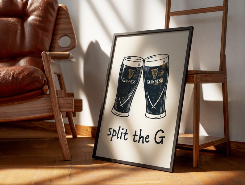 May include: A framed print featuring two stylized Guinness pint glasses. The glasses are black and white with gold accents and the Guinness logo. The phrase "split the G" is written in black script below the glasses.