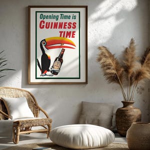 Puede incluir: P&oacute;ster vintage enmarcado de "Guinness Time" con un tuc&aacute;n sosteniendo una botella de Guinness. El p&oacute;ster tiene un fondo blanco con texto verde y rojo. La habitaci&oacute;n incluye una silla de mimbre, un coj&iacute;n de suelo y jarrones decorativos.