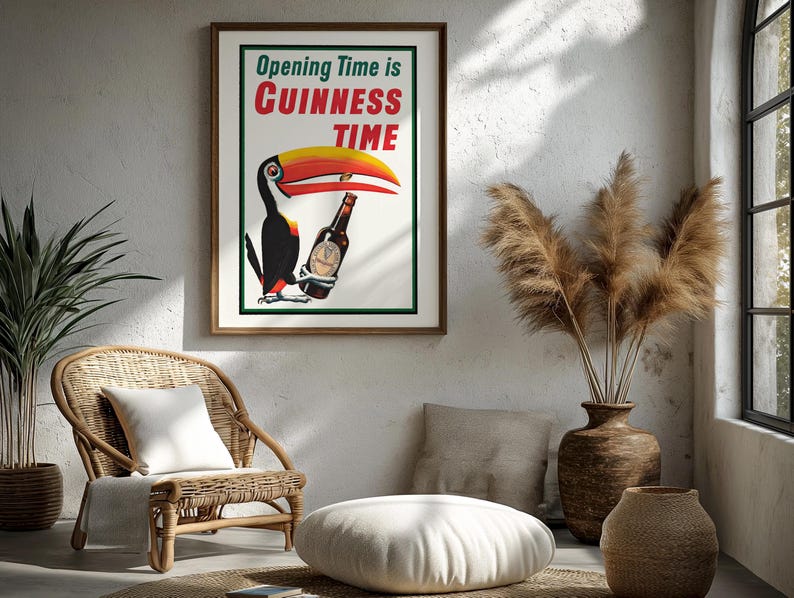 Puede incluir: P&oacute;ster vintage enmarcado de "Guinness Time" con un tuc&aacute;n sosteniendo una botella de Guinness. El p&oacute;ster tiene un fondo blanco con texto verde y rojo. La habitaci&oacute;n incluye una silla de mimbre, un coj&iacute;n de suelo y jarrones decorativos.