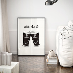 May include: Black and white framed print featuring two Guinness pint glasses with the text "split the G". The print is displayed in a modern living room setting, with a white sofa and decorative elements.