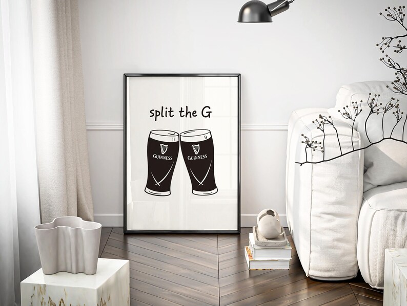 May include: Black and white framed print featuring two Guinness pint glasses with the text "split the G". The print is displayed in a modern living room setting, with a white sofa and decorative elements.