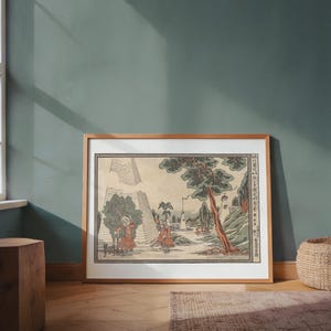 May include: A framed Japanese woodblock print featuring a landscape with figures in red robes, a large tree, and a pagoda. The print has a light brown wooden frame and is displayed on a wooden floor.