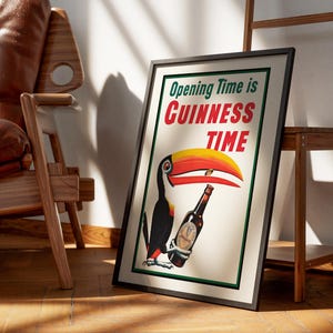 Puede incluir: P&oacute;ster enmarcado con borde negro que presenta un tuc&aacute;n sosteniendo una botella de Guinness. El p&oacute;ster dice "Opening Time is Guinness Time" en texto verde y rojo. La imagen est&aacute; apoyada contra una escalera de madera y una silla de cuero marr&oacute;n.