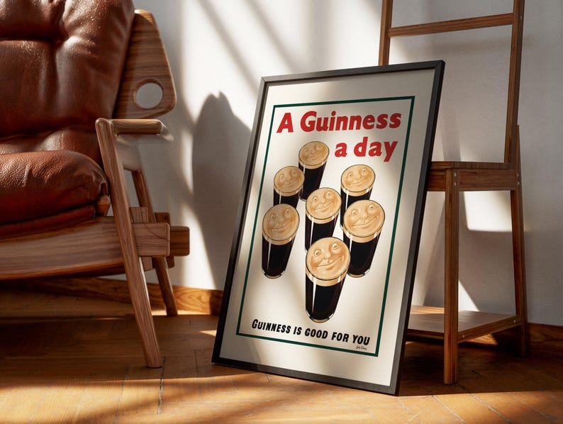 May include: Framed vintage-style poster with the text "A Guinness a day" and "Guinness is good for you." The poster features cartoon pints of Guinness with smiling faces. The poster is displayed on a wooden floor, leaning against a wall.