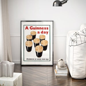May include: Framed vintage Guinness advertisement featuring six pints of stout with creamy foam. The poster has red and white text that reads "A Guinness a day" and "Guinness is good for you."