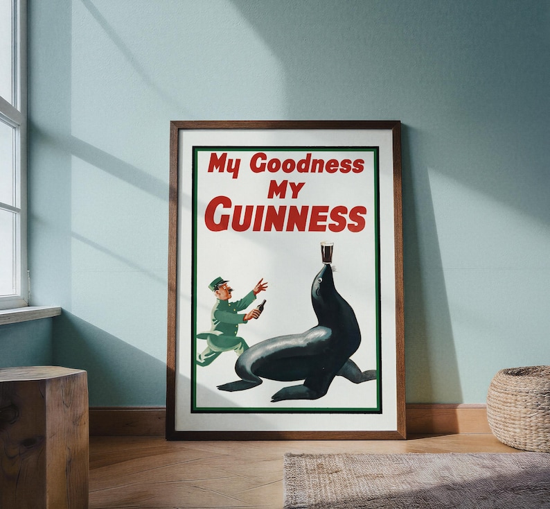 May include: A framed vintage Guinness advertisement. The poster features a seal balancing a pint of Guinness on its nose, with a man in a green uniform running towards it. The text "My Goodness My Guinness" is displayed in red and white.