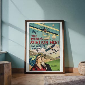 May include: A framed vintage poster advertising "The People's Aviation Meet" in Los Angeles, January 20-28, 1912. The poster features biplanes, dirigibles, and a couple looking up. The poster is in a brown wooden frame.