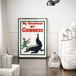 May include: Framed vintage Guinness advertisement featuring a seal balancing a pint of stout. The poster has the text "My Goodness My Guinness" in red and white. A man in a green uniform is depicted running towards the seal. The poster is in a black frame.