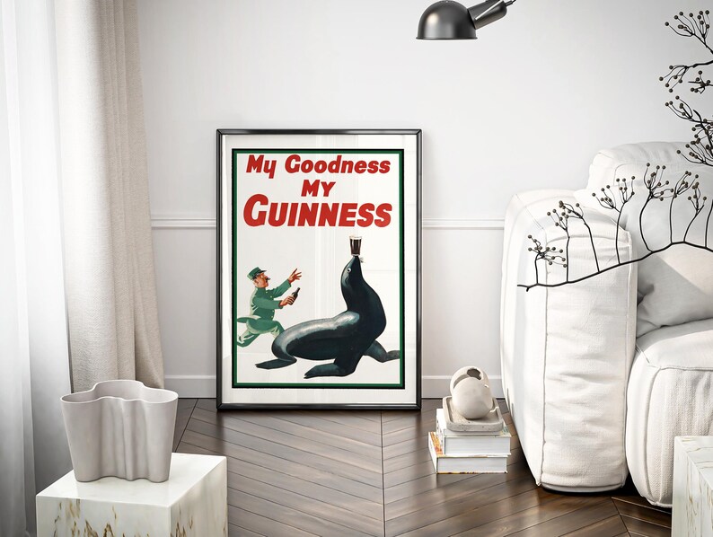 May include: Framed vintage Guinness advertisement featuring a seal balancing a pint of stout. The poster has the text "My Goodness My Guinness" in red and white. A man in a green uniform is depicted running towards the seal. The poster is in a black frame.