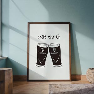 May include: A framed print featuring two Guinness pint glasses with the text "split the G". The glasses are black with white accents and the Guinness logo. The frame is brown.