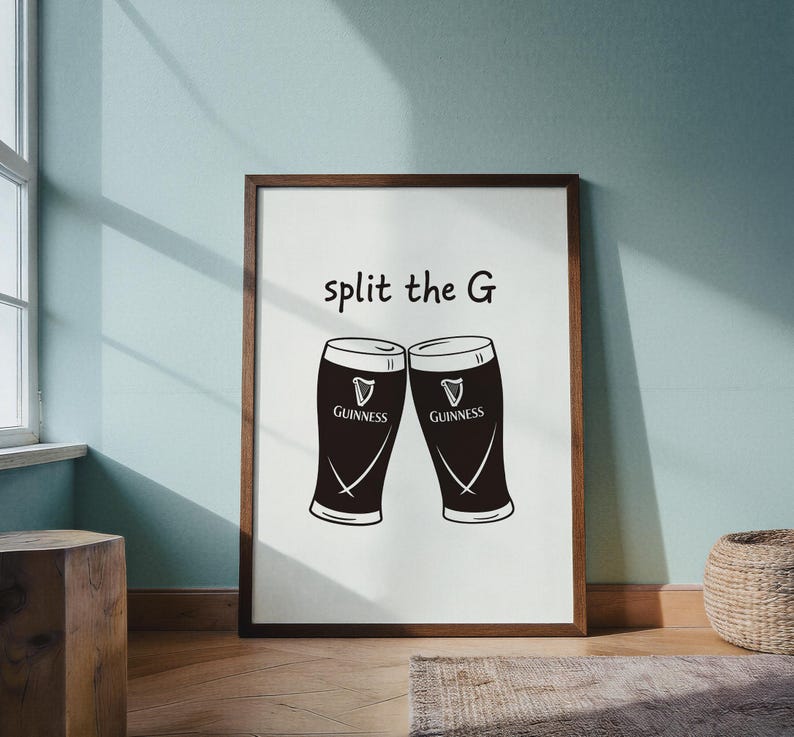 May include: A framed print featuring two Guinness pint glasses with the text "split the G". The glasses are black with white accents and the Guinness logo. The frame is brown.