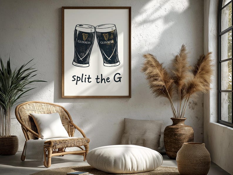 May include: A framed print featuring two Guinness pint glasses with the text "split the G". The artwork is in black and white, with the Guinness logo visible on each glass. The print is displayed in a well-lit room with a wicker chair and decorative vase.