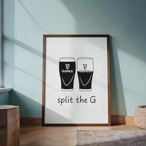 May include: A framed print featuring two Guinness pint glasses, one filled and one empty, with the text "split the G" in a black font. The Guinness logo is visible on each glass. The frame is brown.