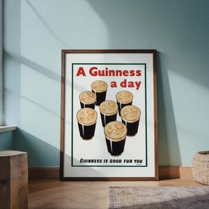 May include: A framed vintage advertisement for Guinness stout. The poster features seven smiling pints of Guinness with the text "A Guinness a day" and "Guinness is good for you" in red and black.