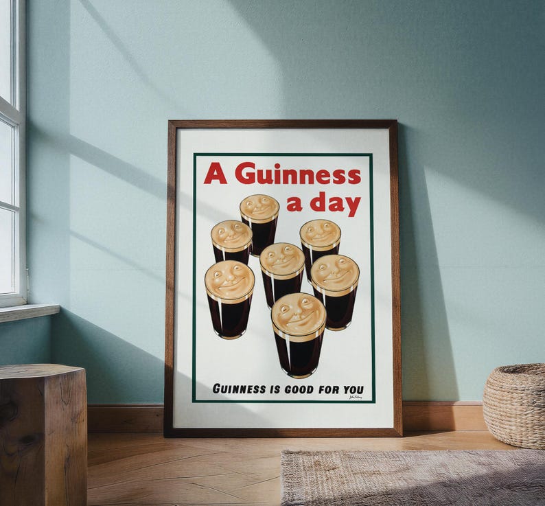 May include: A framed vintage advertisement for Guinness stout. The poster features seven smiling pints of Guinness with the text "A Guinness a day" and "Guinness is good for you" in red and black.