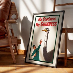 May include: Framed vintage Guinness advertisement featuring a cartoon ostrich with a smiling face and a man in a green uniform. The text "My Goodness My GUINNESS" is displayed in red. The poster is leaning against a wall near a wooden chair.