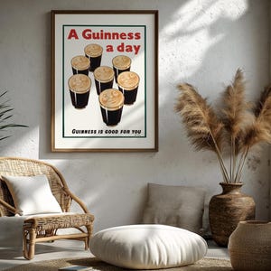 May include: A framed print with the text "A Guinness a day" and "Guinness is good for you." The print features six pints of Guinness. The print is in a room with a wicker chair, a white pillow, and a vase with dried plants.