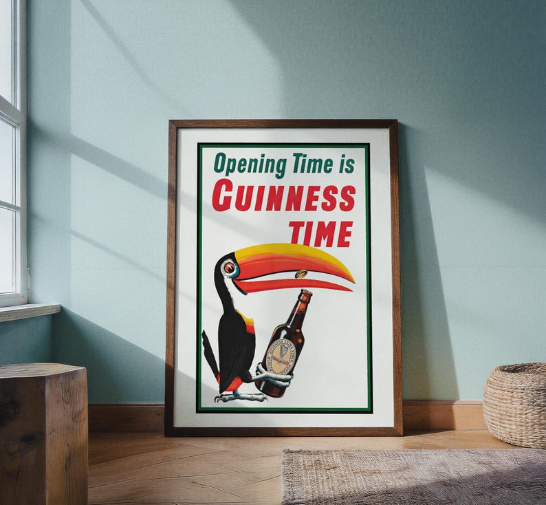Puede incluir: P&oacute;ster vintage enmarcado de Guinness con un tuc&aacute;n sosteniendo una botella de cerveza Guinness. El p&oacute;ster tiene el texto "Opening Time is Guinness Time" en rojo y verde. El tuc&aacute;n tiene un gran pico amarillo y rojo.