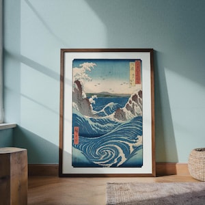 May include: Framed print of a Japanese woodblock depicting a swirling ocean scene with crashing waves and a distant island. The artwork features shades of blue, white, and brown, with Japanese text in the upper right and lower left corners.