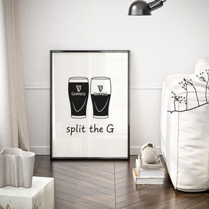 May include: Black and white framed print featuring two Guinness pint glasses. The text "split the G" is below the glasses. The print is displayed in a modern living room setting with a white sofa and decorative elements.
