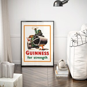 May include: A framed vintage Guinness advert. The poster shows a green steamroller with the text "GUINNESS for strength" in red and white. The poster is in a black frame with an orange border, displayed in a modern living room.