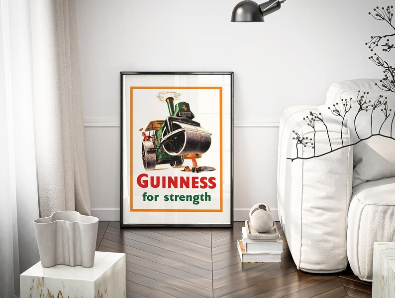May include: A framed vintage Guinness advert. The poster shows a green steamroller with the text "GUINNESS for strength" in red and white. The poster is in a black frame with an orange border, displayed in a modern living room.