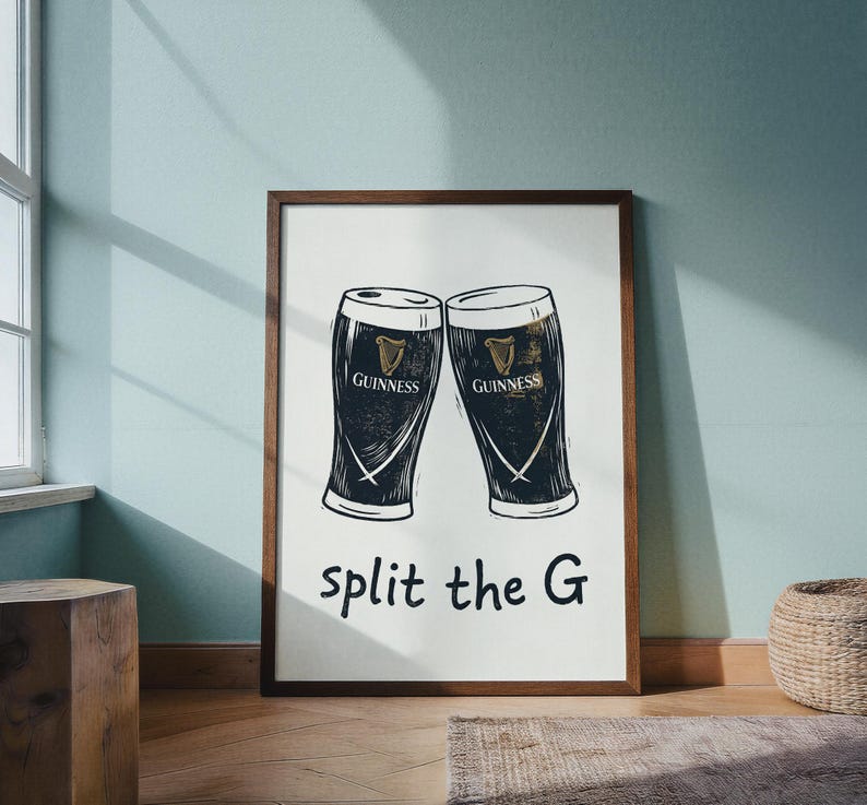 May include: A framed print featuring two Guinness pint glasses, rendered in black and white. The Guinness logo is visible on each glass. The phrase "split the G" is written below the glasses in a simple font. The frame is a dark brown color.